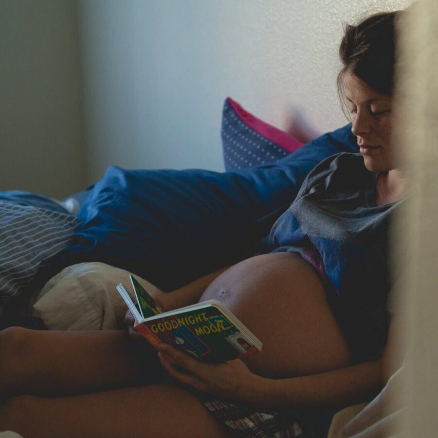 pregnant woman sitting on bed and reading book